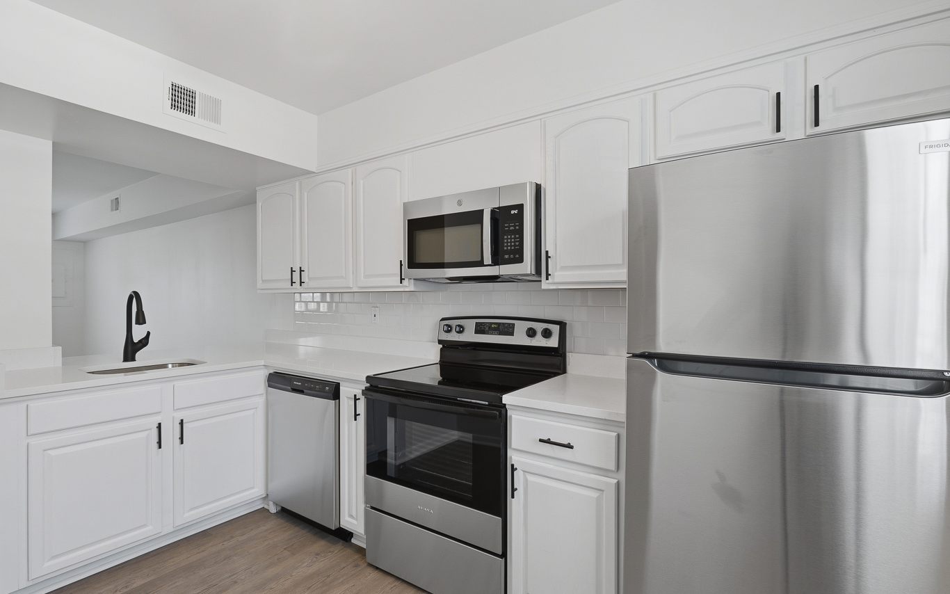 A renovated kitchen with white cabinets, white counters and stainless appliances