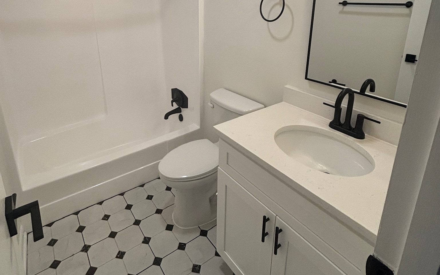 A renovated bathroom with a white vanity, black fixtures and patterned tile floor